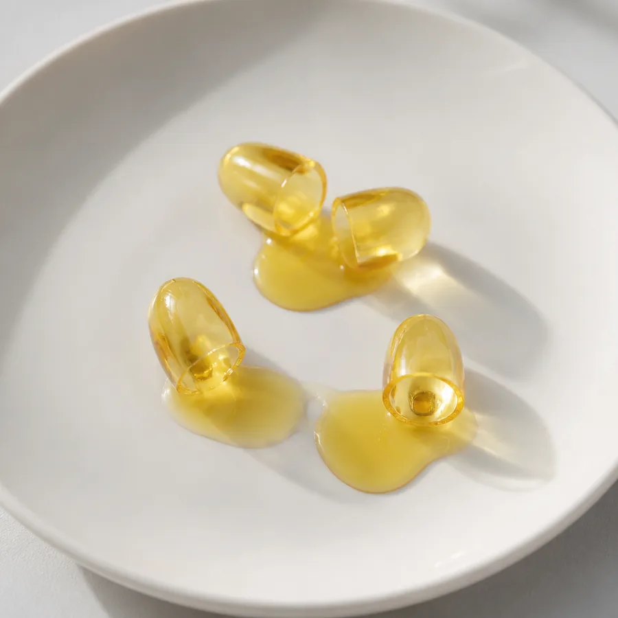 Open softgel capsules with golden oil on ceramic